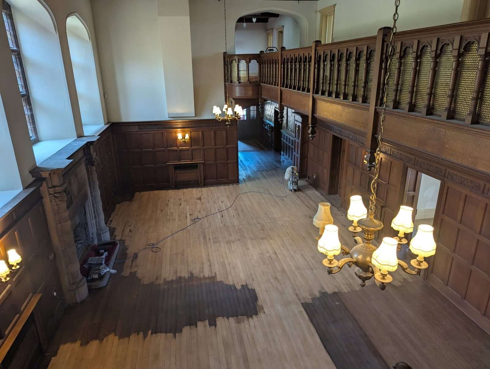 Higham Hall oak floor partway through sanding, with the sanding machine and dust extraction hose at work in the hall