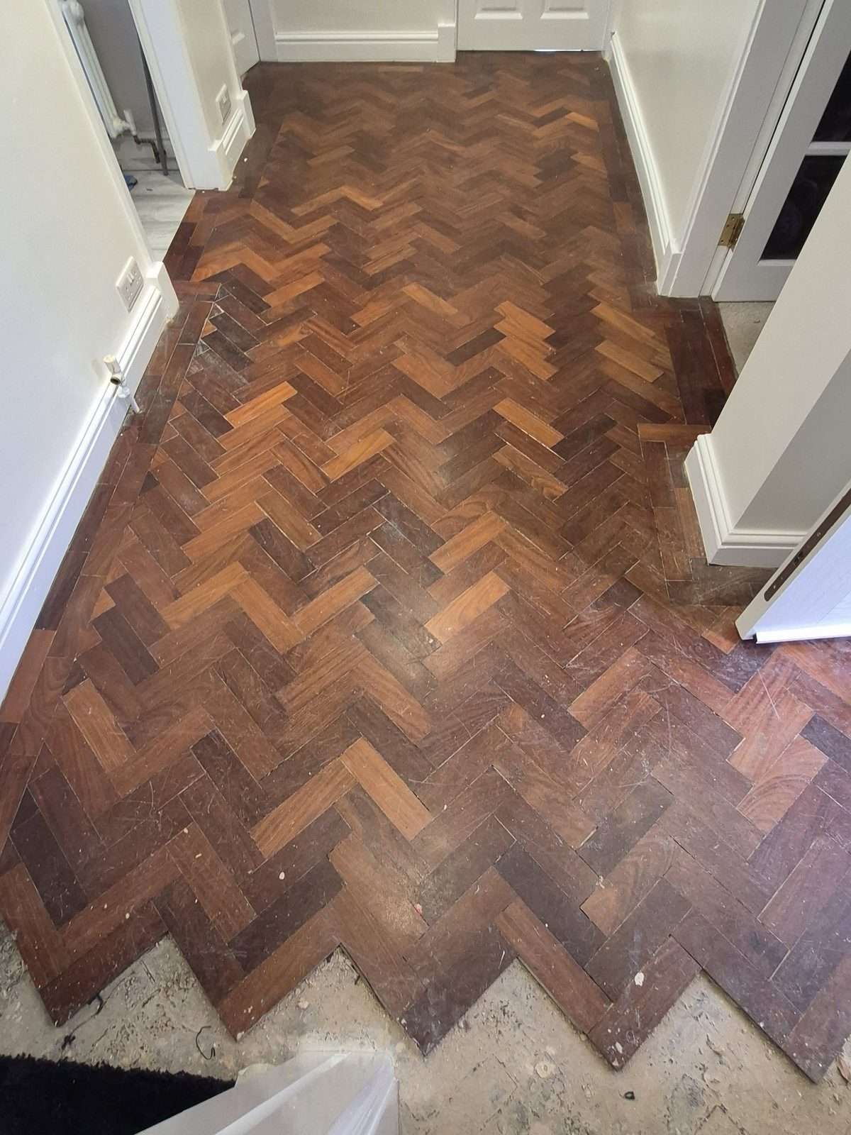 Iroko herringbone parquet hallway before refinishing, with a dark worn finish and scratched blocks