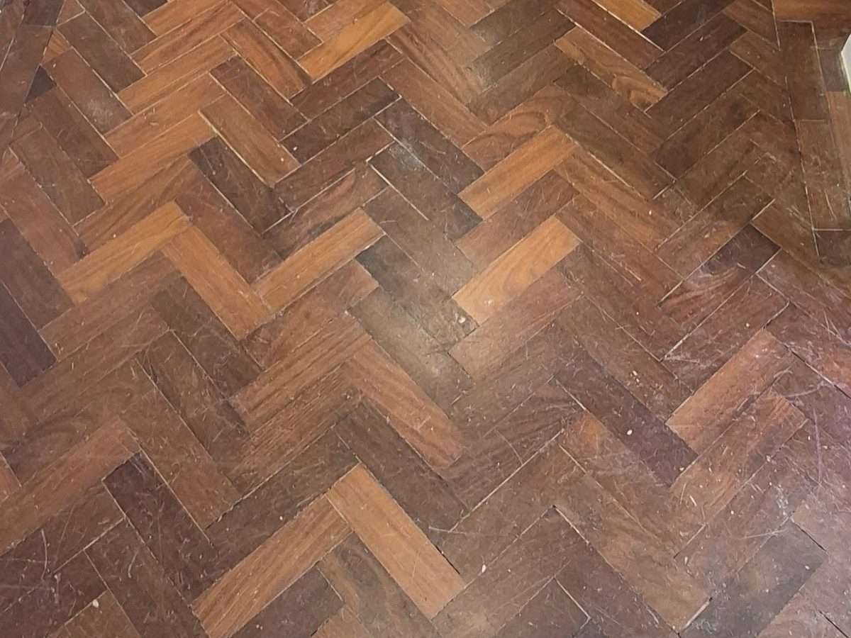 Close up of Iroko herringbone parquet before refinishing, showing scratches and a worn dark finish